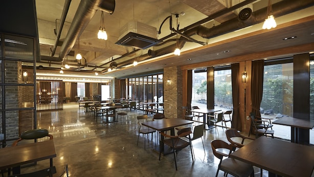 Un comedor interior amplio con varias mesas y sillas, ventanas grandes y conductos expuestos en el techo.