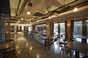 Un comedor interior amplio con varias mesas y sillas, ventanas grandes y conductos expuestos en el techo.