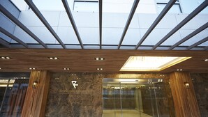 La entrada del Hotel Royal Square, con un diseño moderno, presenta un ascensor de vidrio, un panel de madera y un tragaluz.