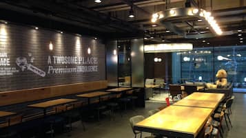 Una cafetería moderna con paredes de ladrillo, mesas de madera y un mural grande que anuncia café de primera calidad.
