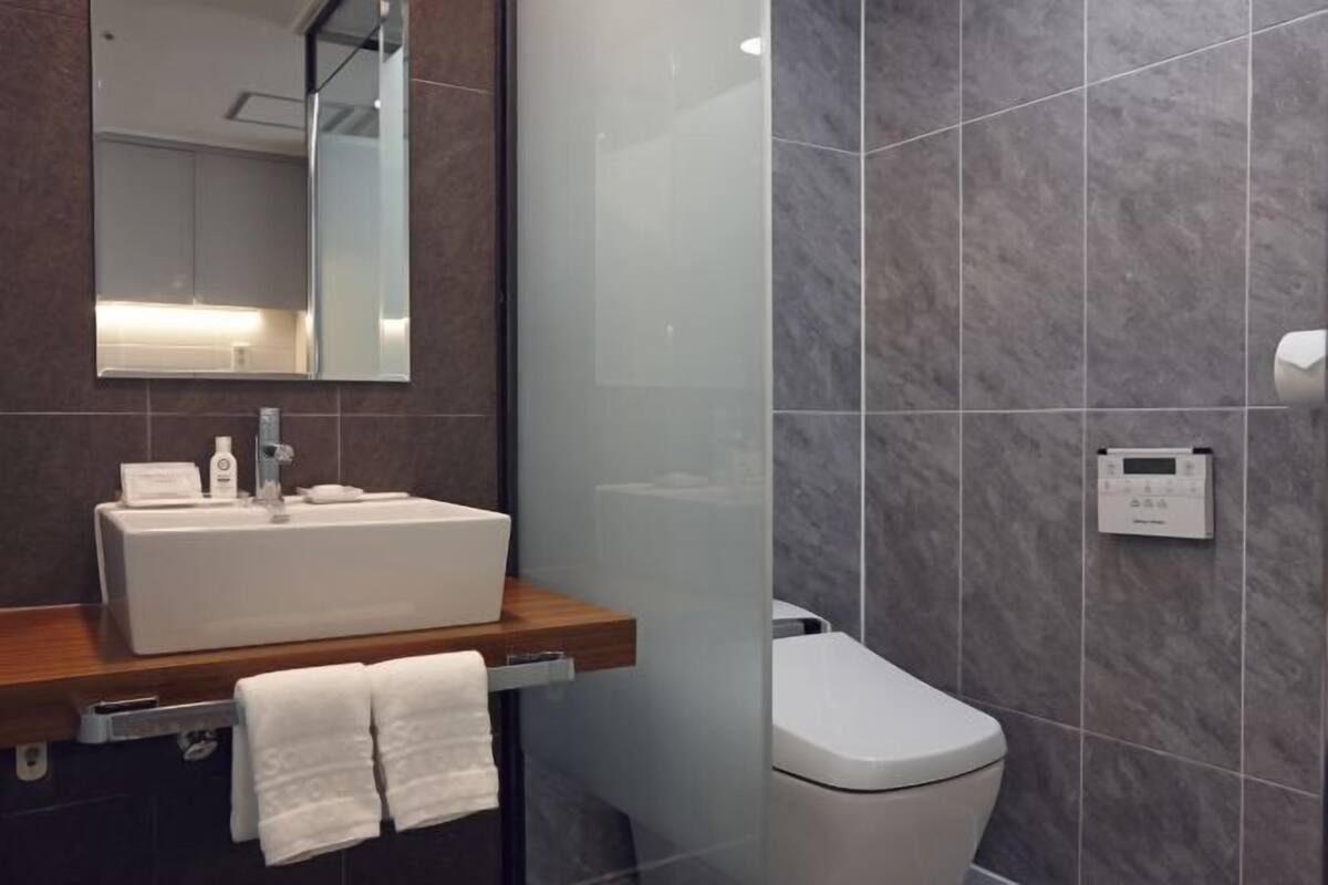 Un baño moderno con un espejo grande, un lavabo blanco y un inodoro.