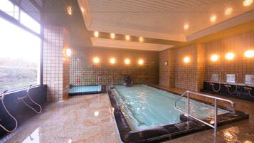A large indoor swimming pool with a tiled wall and a metal railing.