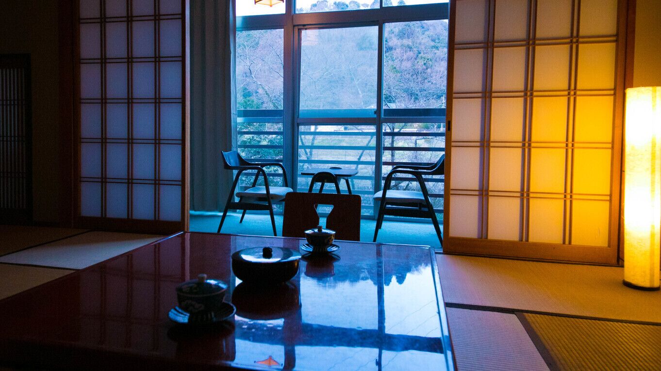 Una habitación tradicional japonesa con suelo de tatami, una mesa baja con un juego de té y puertas correderas.
