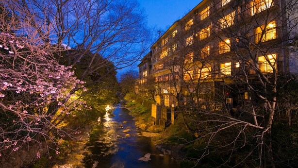 A riverside building with multiple floors, a stone pathway, and flowering trees. - Seishounagon (Tsu)