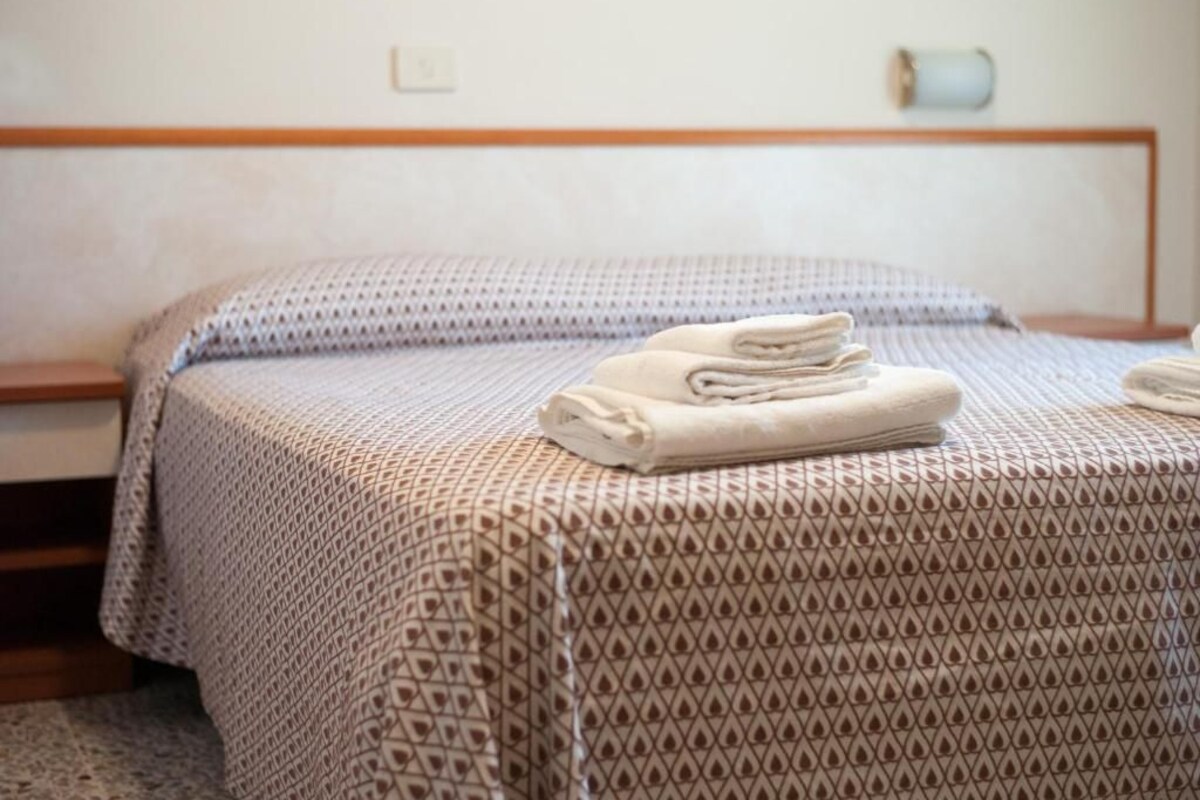 Una cama bien hecha con un edredón estampado y almohadas, una toalla doblada sobre la cama y un cabecero de madera.