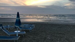 A beach with lounge chairs and umbrellas, a calm sea, and a sunset sky. - Hotel Stella del Mare (Cervia)