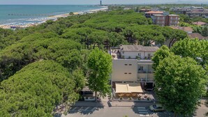 An aerial view of a coastal area with a beach, dense green trees, and residential buildings. - Hotel Stella del Mare (Cervia)