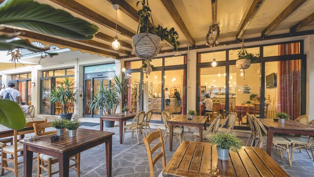 An outdoor cafe with wooden tables and chairs, potted plants, and hanging baskets. - Hotel Stella del Mare (Cervia)