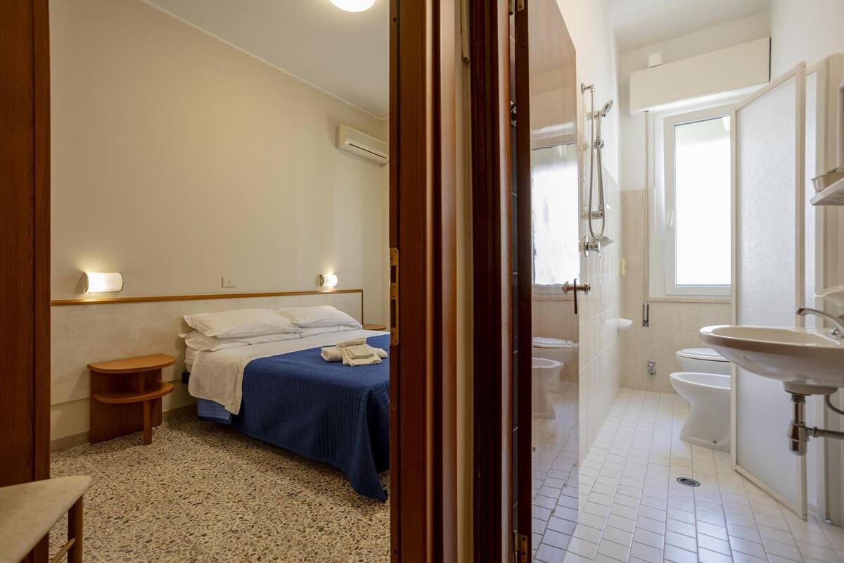 Un dormitorio con cama, mesita de noche y baño con lavabo e inodoro.