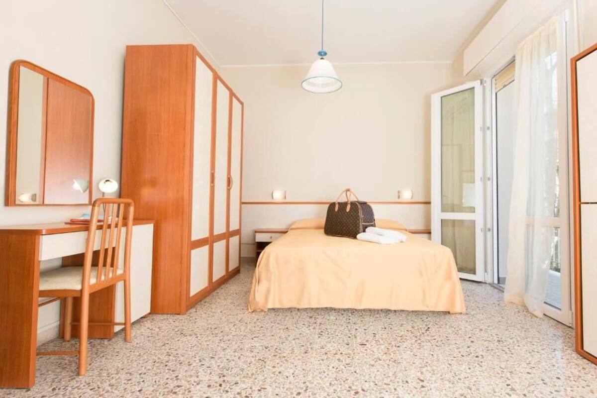 Una habitación de hotel con una cama, un escritorio con silla, un armario y una puerta corrediza de vidrio.