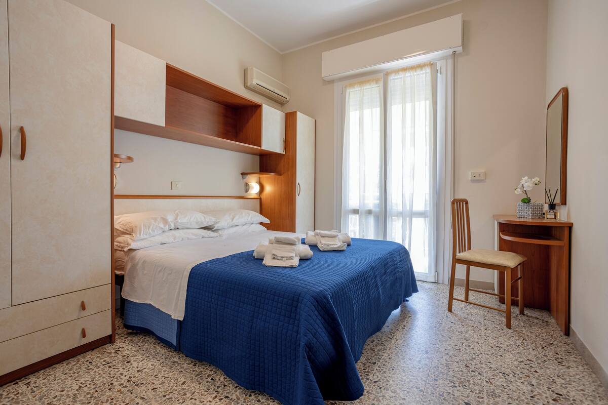 Un dormitorio con cama, una silla, un escritorio y un espejo.