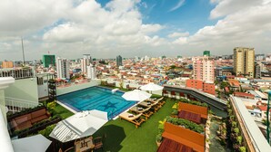 A rooftop pool area with lounge chairs and umbrellas, surrounded by a cityscape. - Le Mont Hotel (Phnom Penh)