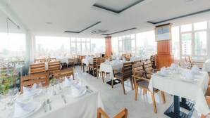 A restaurant with multiple tables set for dining, large windows offering a city view, and a modern ceiling design. - Le Mont Hotel (Phnom Penh)