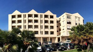 Un hotel de varios pisos con un diseño arquitectónico moderno, que incluye un estacionamiento con varios coches y palmeras en primer plano.