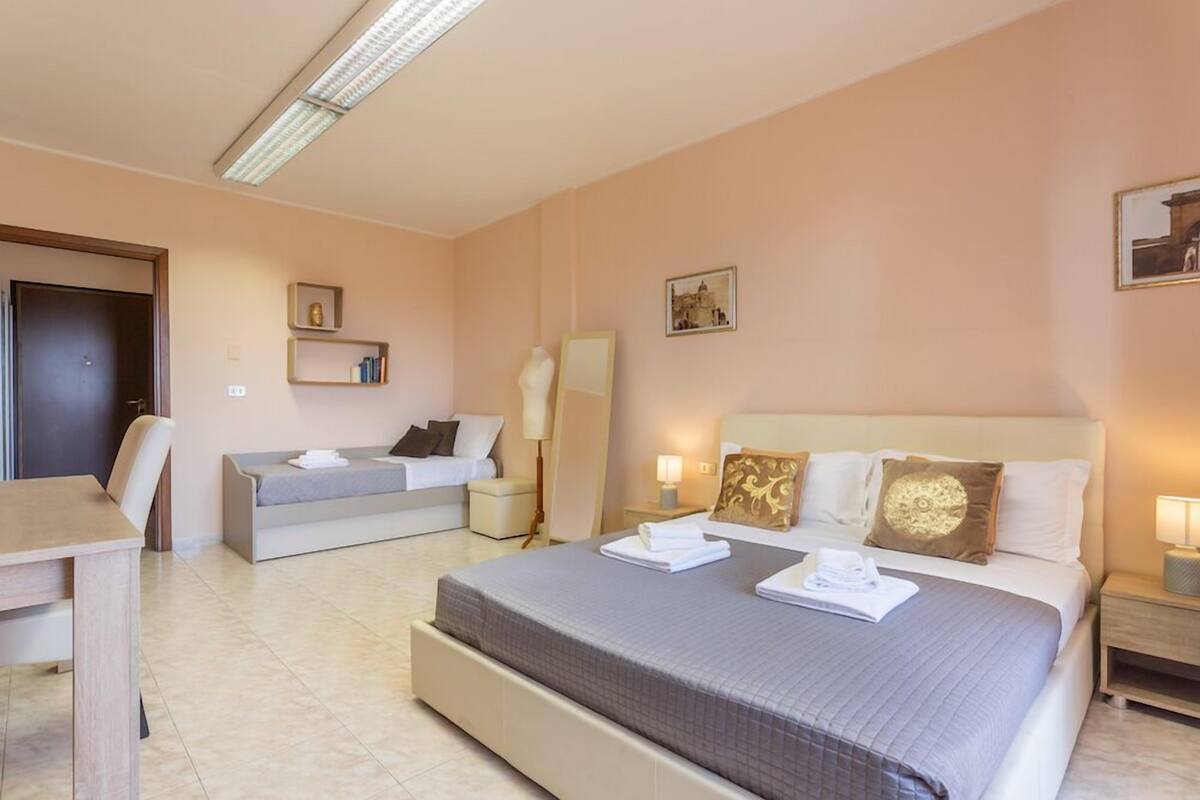 A hotel room with a large bed, a sofa bed, a desk, and a chair.