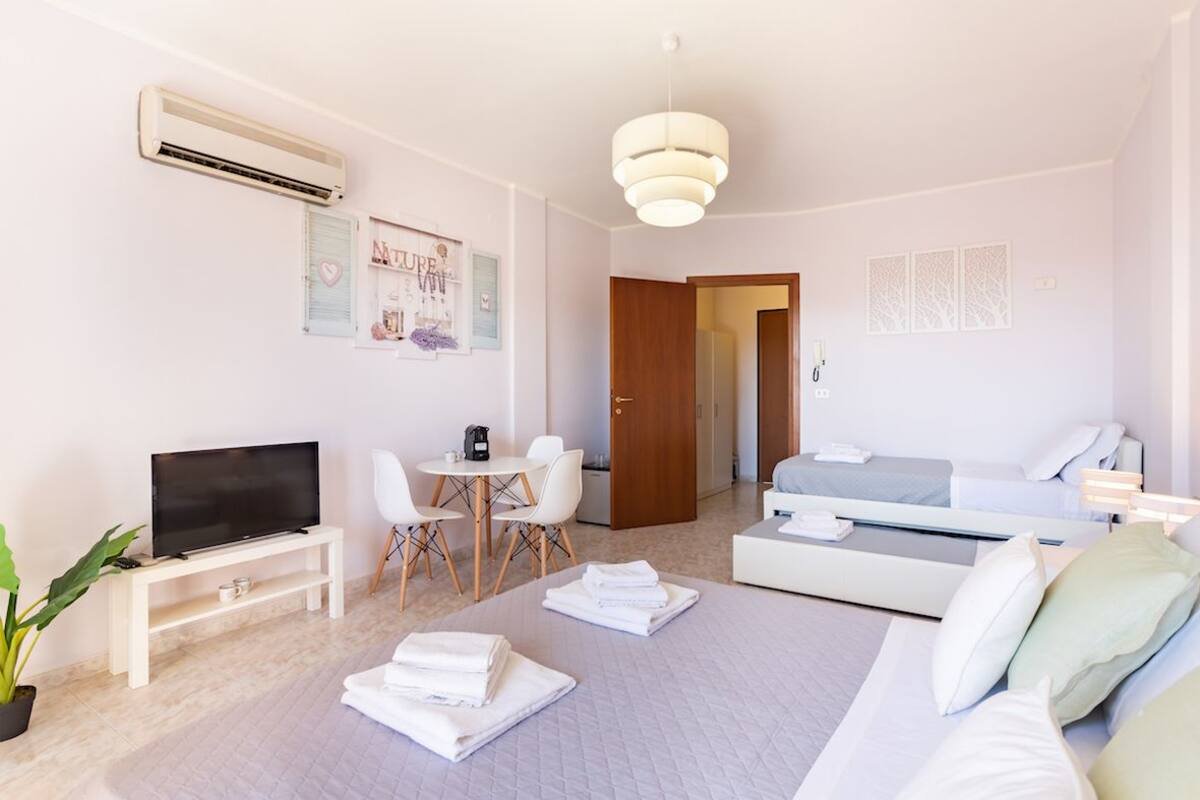 A modern hotel room with a flat-screen TV, a small dining table, a sofa, and a bed.
