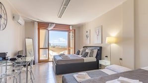 Una habitación de hotel moderna con dos camas, un escritorio con sillas, un ventanal con vistas y un ventilador de techo.