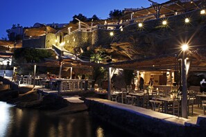 A waterfront restaurant with outdoor seating, stone walls, and a view of the water. - Anastasia Resort by Spilia (Mykonos)