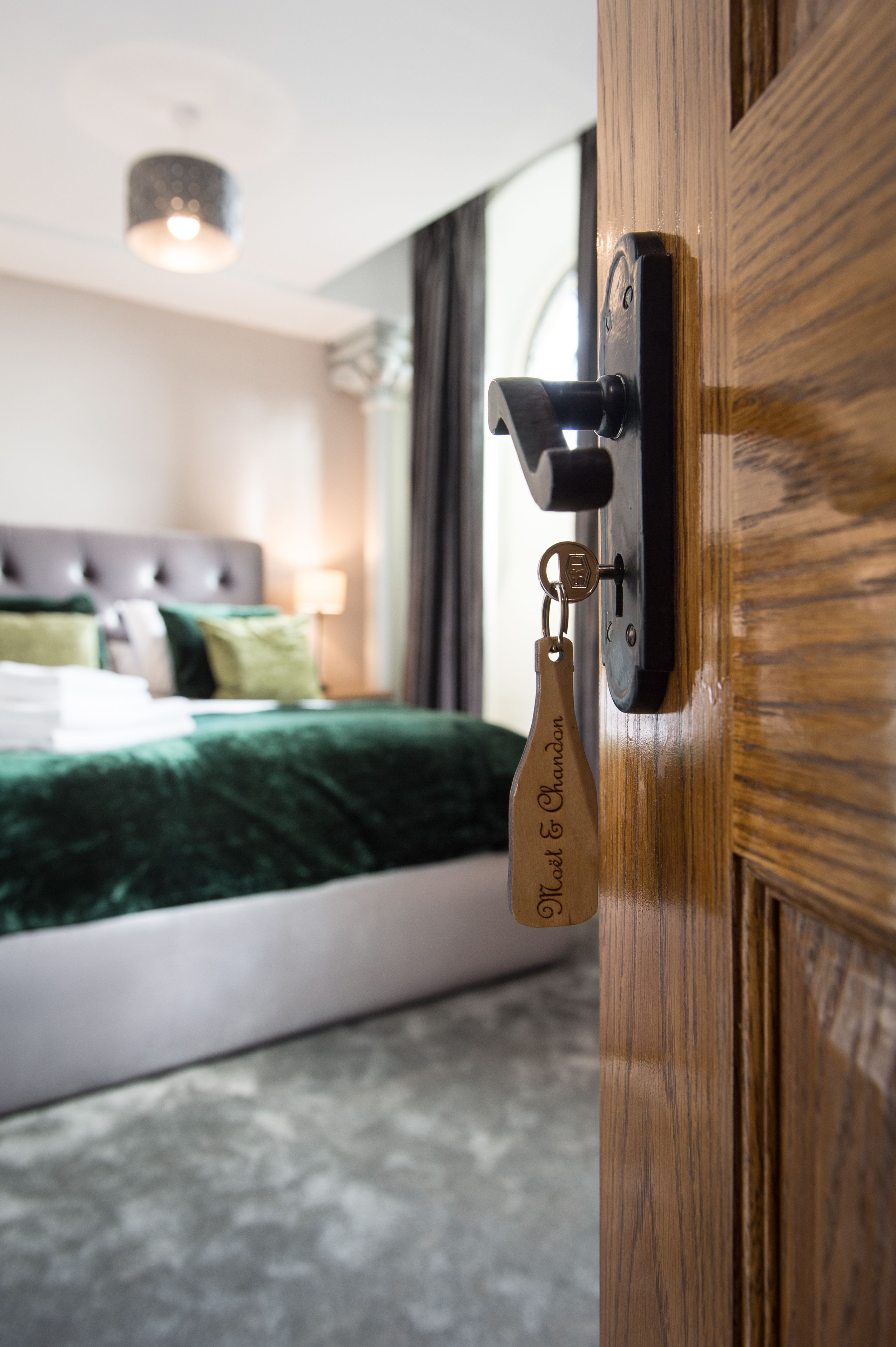 A hotel room with a wooden door, a keychain, and a bed with a green bedspread.