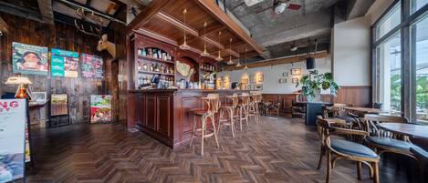 A bar area with wooden floors, bar stools, and a wooden counter with bottles.