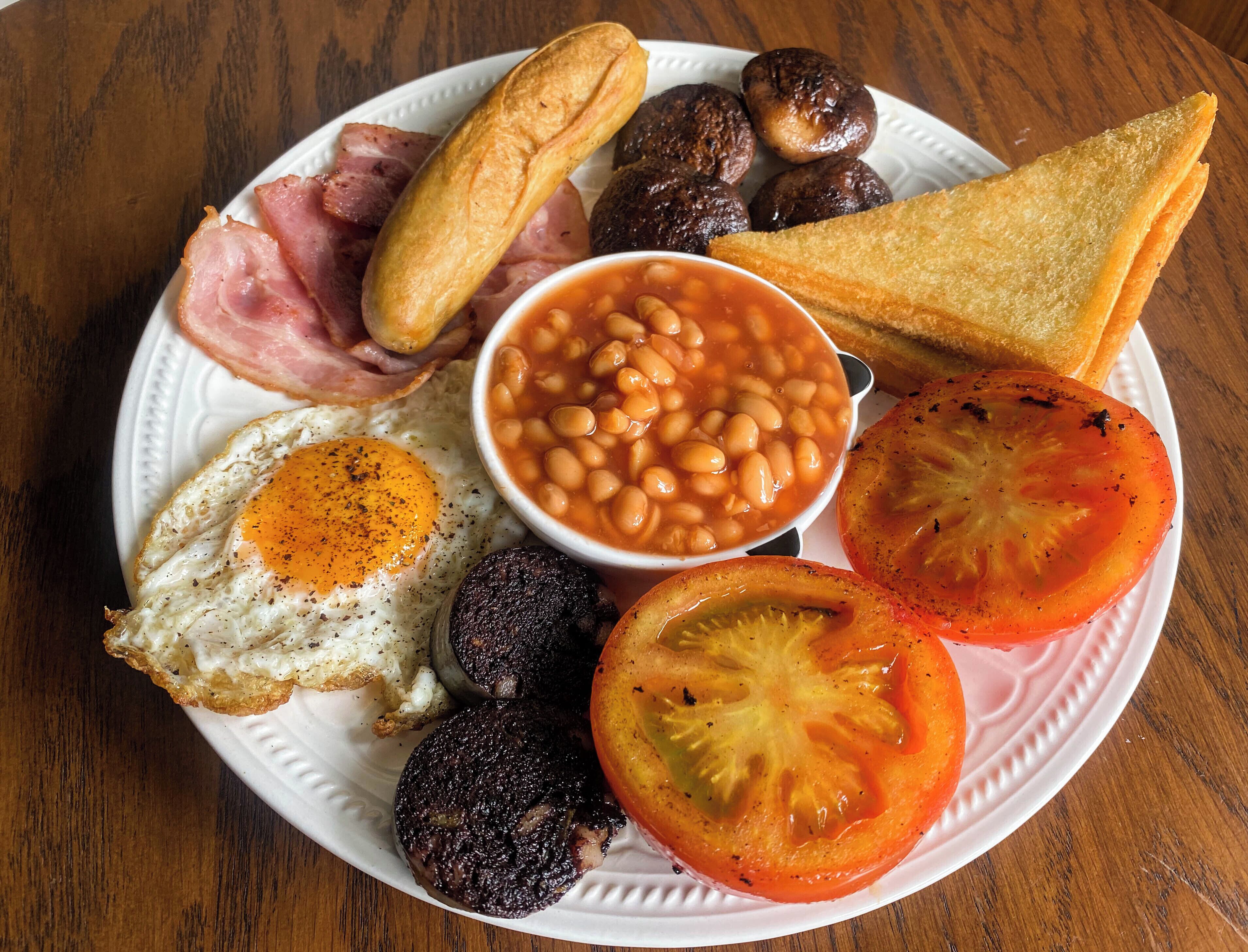 A plate of breakfast food including eggs, beans, tomatoes, mushrooms, and toast.