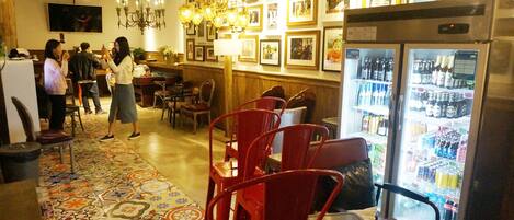 A restaurant interior with a patterned floor, red chairs, a refrigerator with beverages, and framed pictures on the wall.