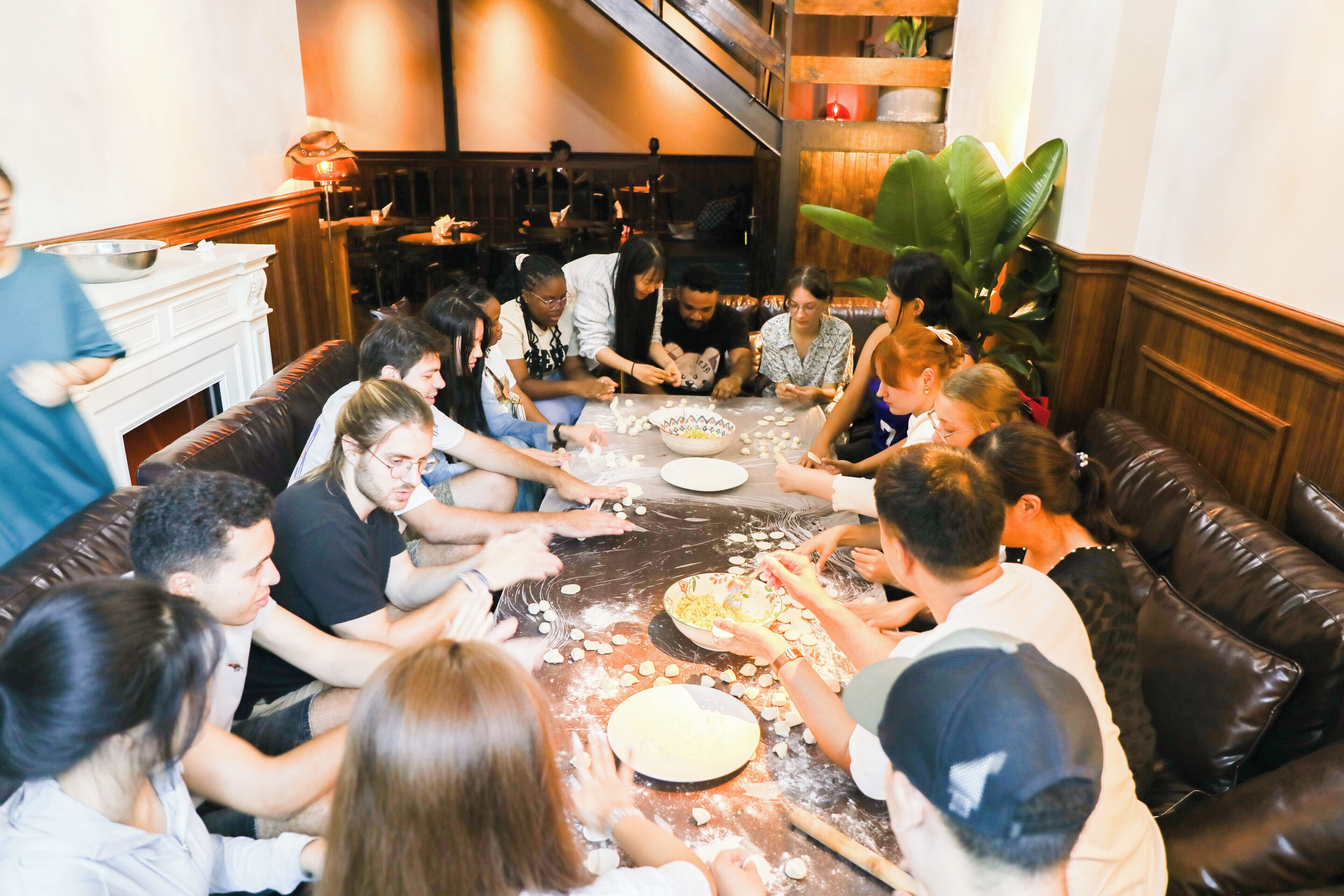 A group of people gathered around a table in a cozy, well-lit room with a fireplace and comfortable seating.