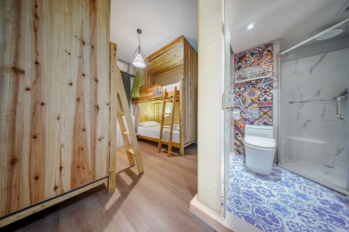 A wooden bunk bed with a ladder, a shower with a glass door, and a tiled bathroom floor.