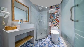 Un baño moderno con cabina de ducha de vidrio, un lavabo blanco con repisa de madera y una pared de azulejos coloridos.