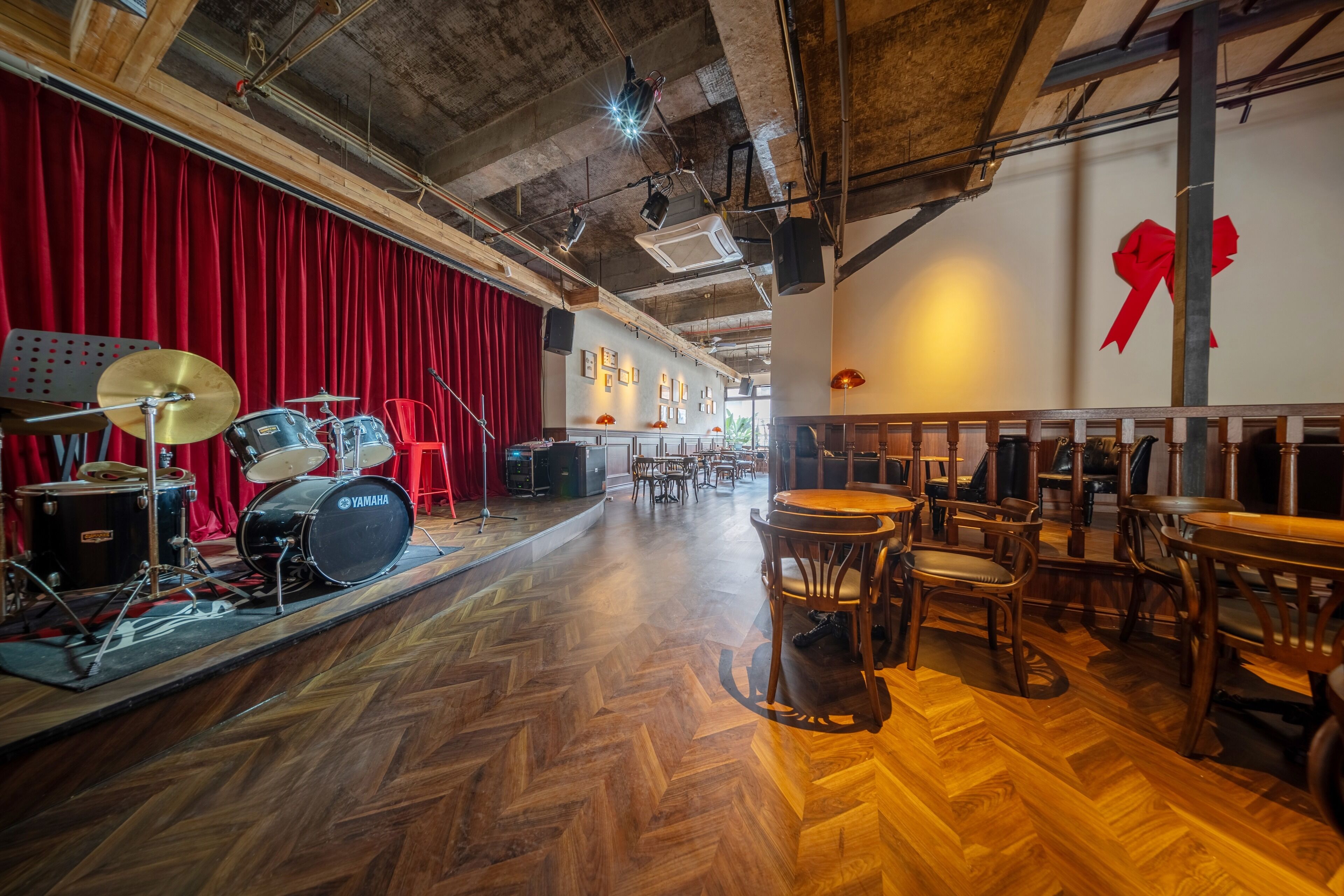 A spacious room with a red curtain backdrop, a drum set, and wooden furniture.