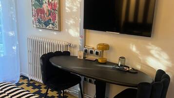 A hotel room with a bed, a table with chairs, a flat-screen TV, a radiator, and a painting on the wall.