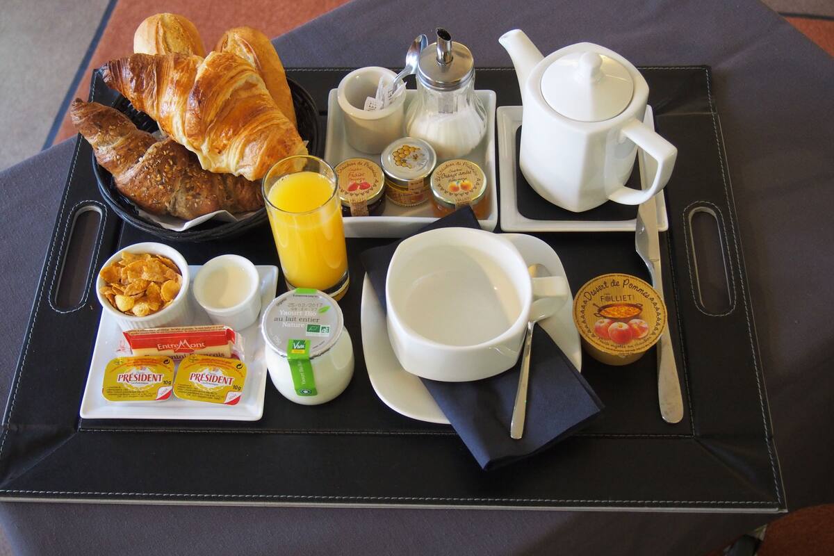 A breakfast tray with croissants, orange juice, yogurt, and jam.