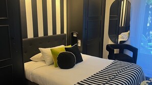 A hotel room with a large bed, striped wall paneling, two bedside lamps, a mirror, and a patterned floor. - Hôtel du Croisé (Marcq-en-Baroeul)