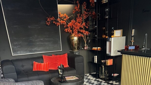 A modern hotel lobby with a checkered floor, a sofa with red cushions, a coffee table, and a vase with orange flowers. - Hôtel du Croisé (Marcq-en-Baroeul)