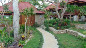 A pathway leading to a traditional-style building with a red roof, surrounded by lush greenery and a stone wall. - Starfish Lembongan (Lembongan Island)