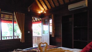 A wooden cabin room with a bed, a window with curtains, and an air conditioning unit. - Starfish Lembongan (Lembongan Island)