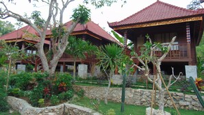 A traditional wooden building with a tiled roof, surrounded by lush greenery and a stone wall. - Starfish Lembongan (Lembongan Island)