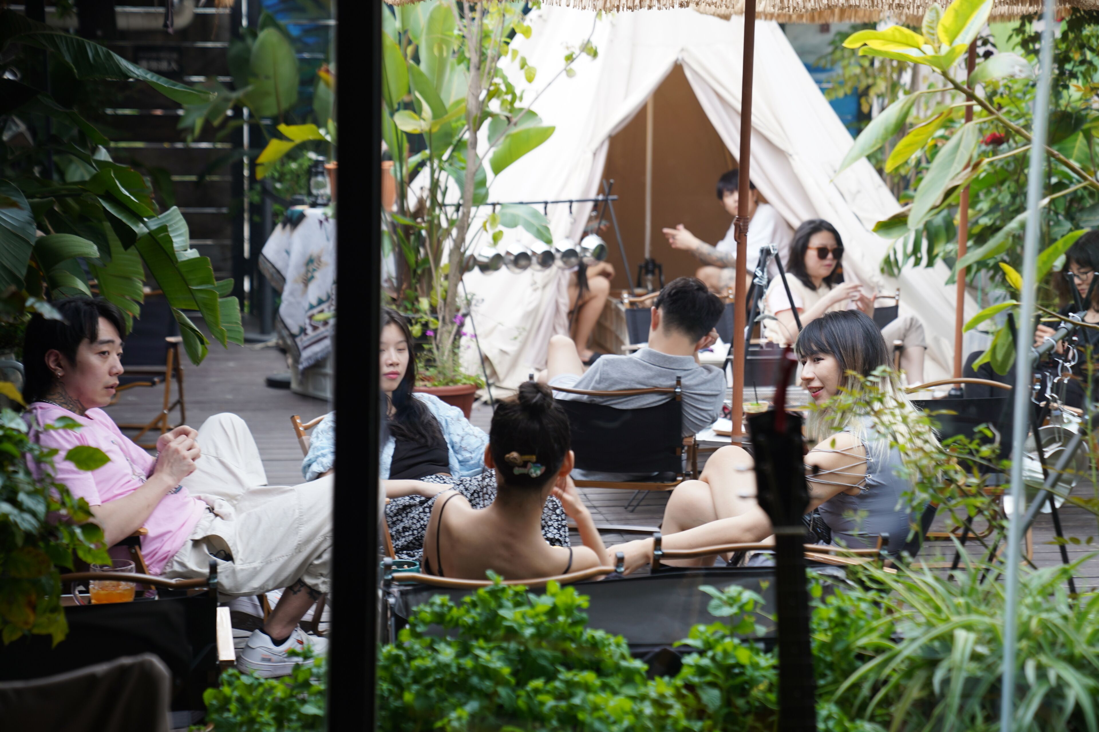 Un espace extérieur aménagé avec des tables et des chaises, entouré d’une végétation luxuriante et abrité par une structure en forme de tente.