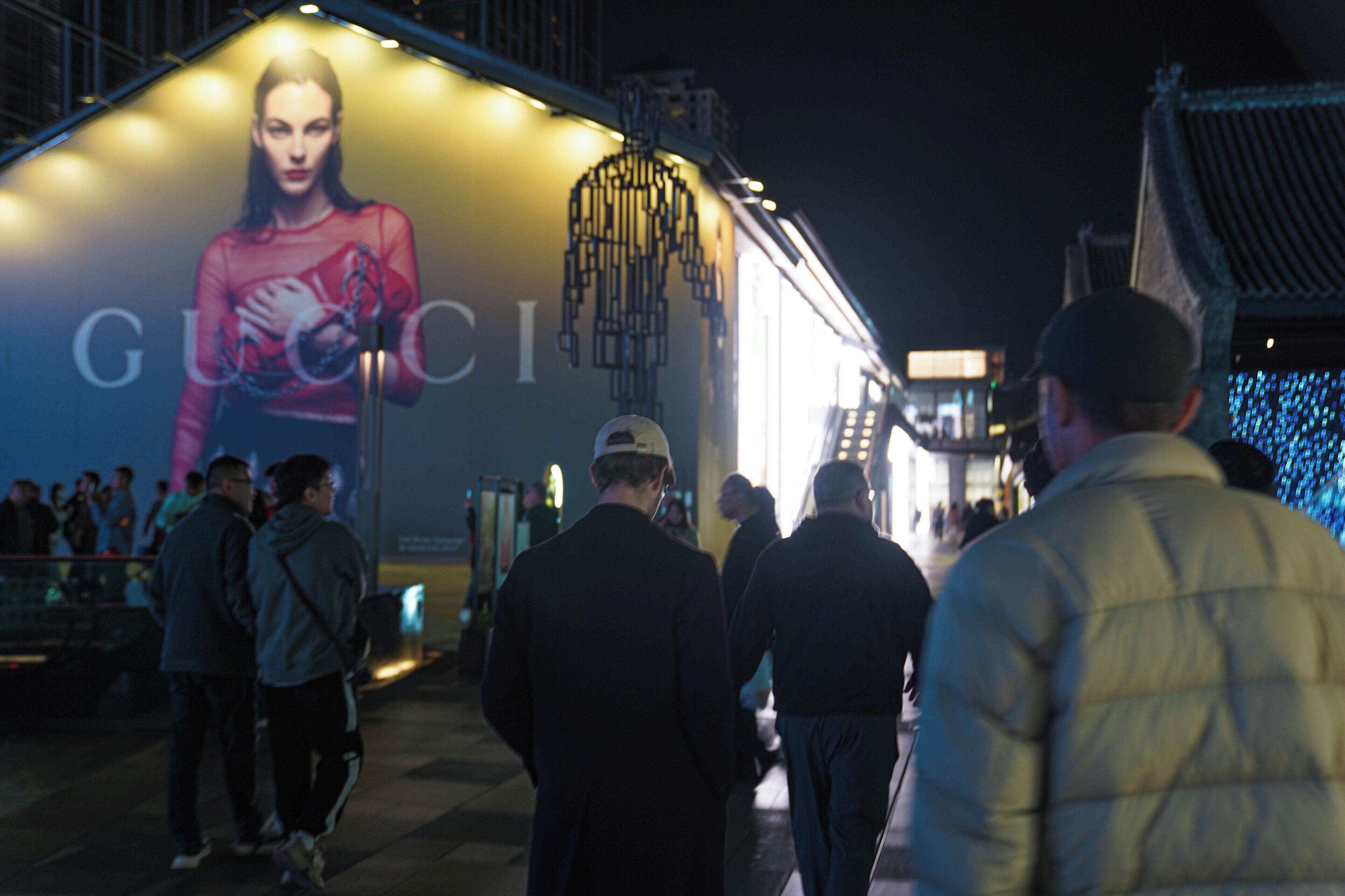 A nighttime urban scene with a large illuminated advertisement for Gucci on a building.