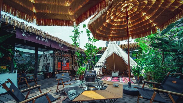 Un espace extérieur aménagé avec des parasols en chaume, un foyer de camp et une tente en arrière-plan.