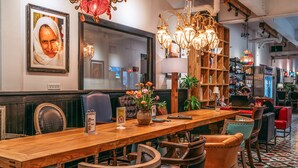 Un restaurant avec une table en bois, des chaises en cuir et un lustre. Il y a un miroir au mur et une bibliothèque contenant divers objets.