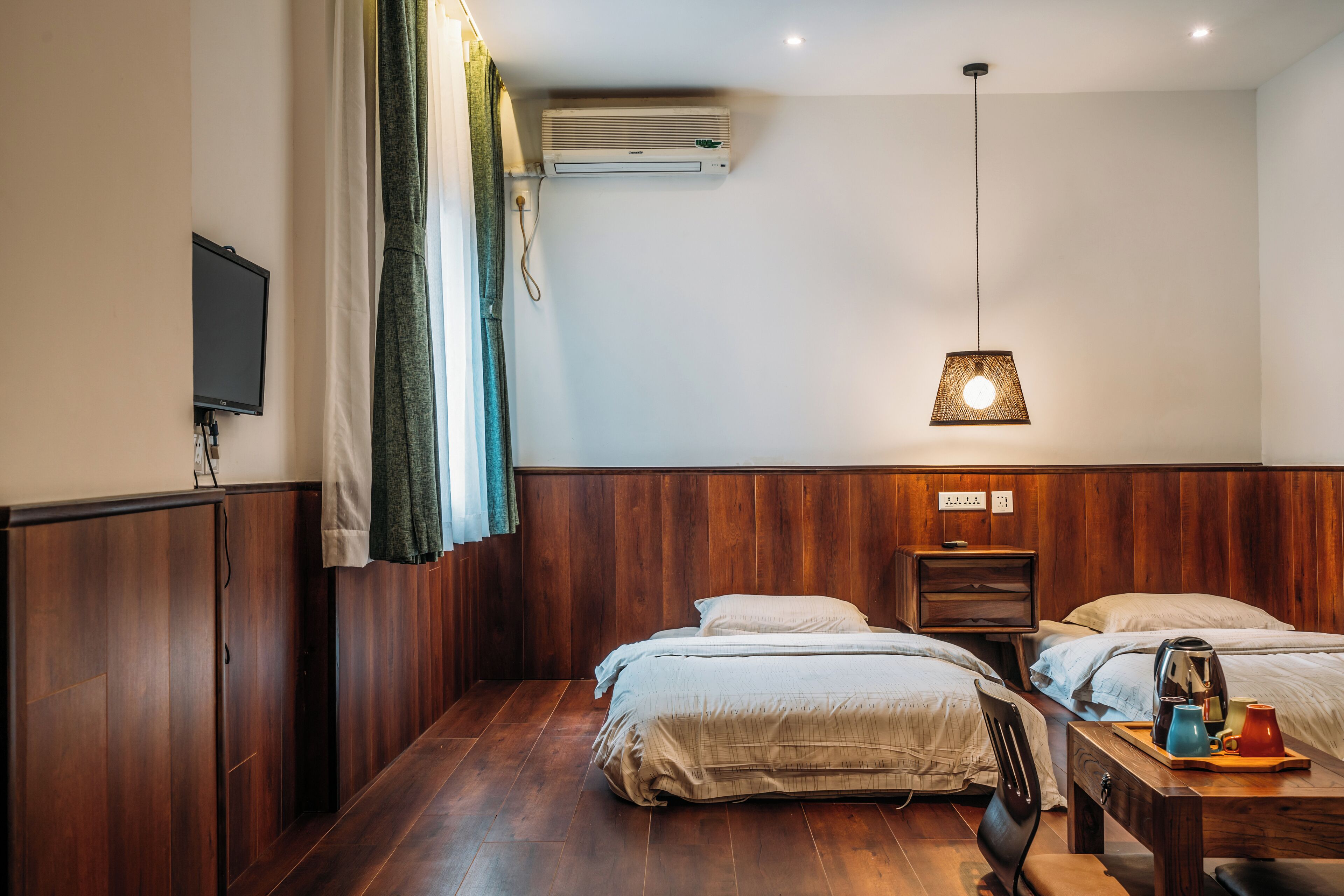A hotel room with wooden paneling, a bed, a bedside table with a lamp, and an air conditioning unit.