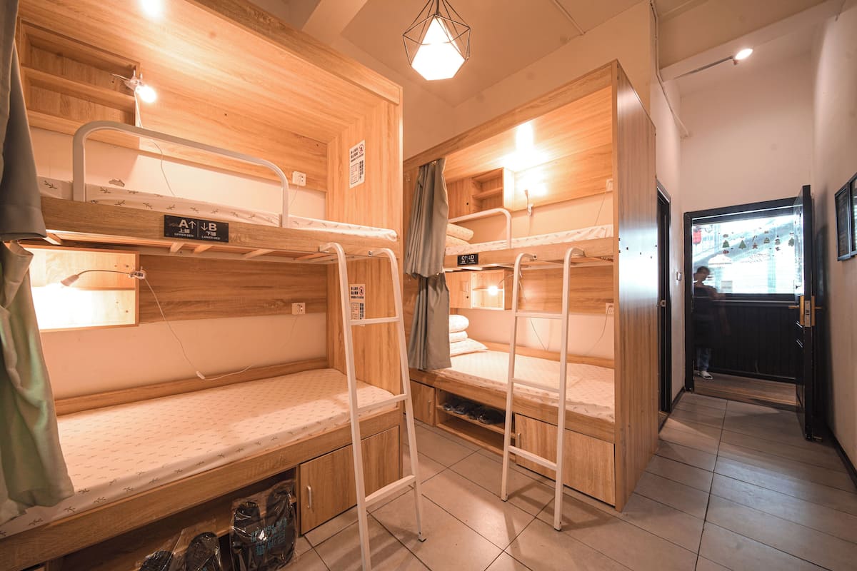 A room with bunk beds, a wooden interior, a door leading outside, and a small shelf with items.