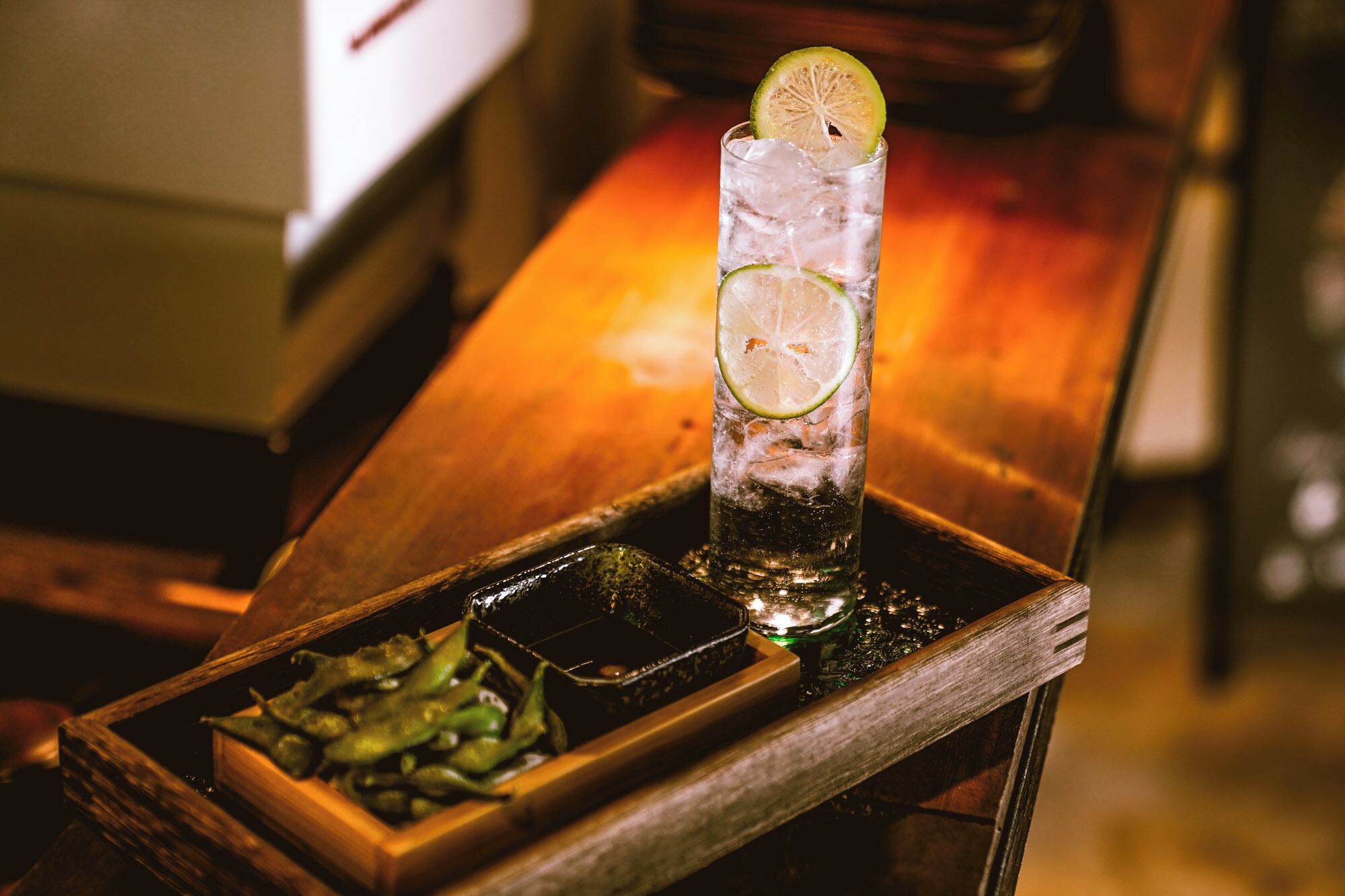 A tall glass with ice and lime slices on a wooden tray.