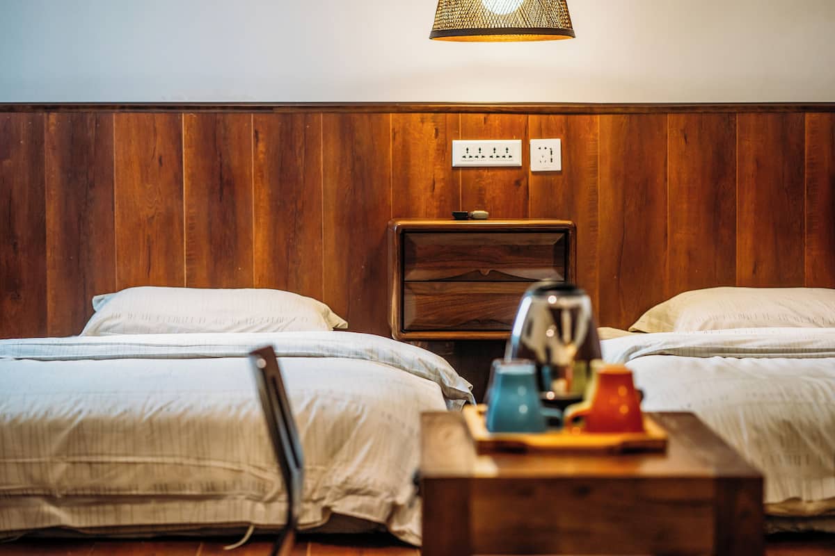 A room with two beds, wooden walls, a nightstand with a lamp, and a power outlet.