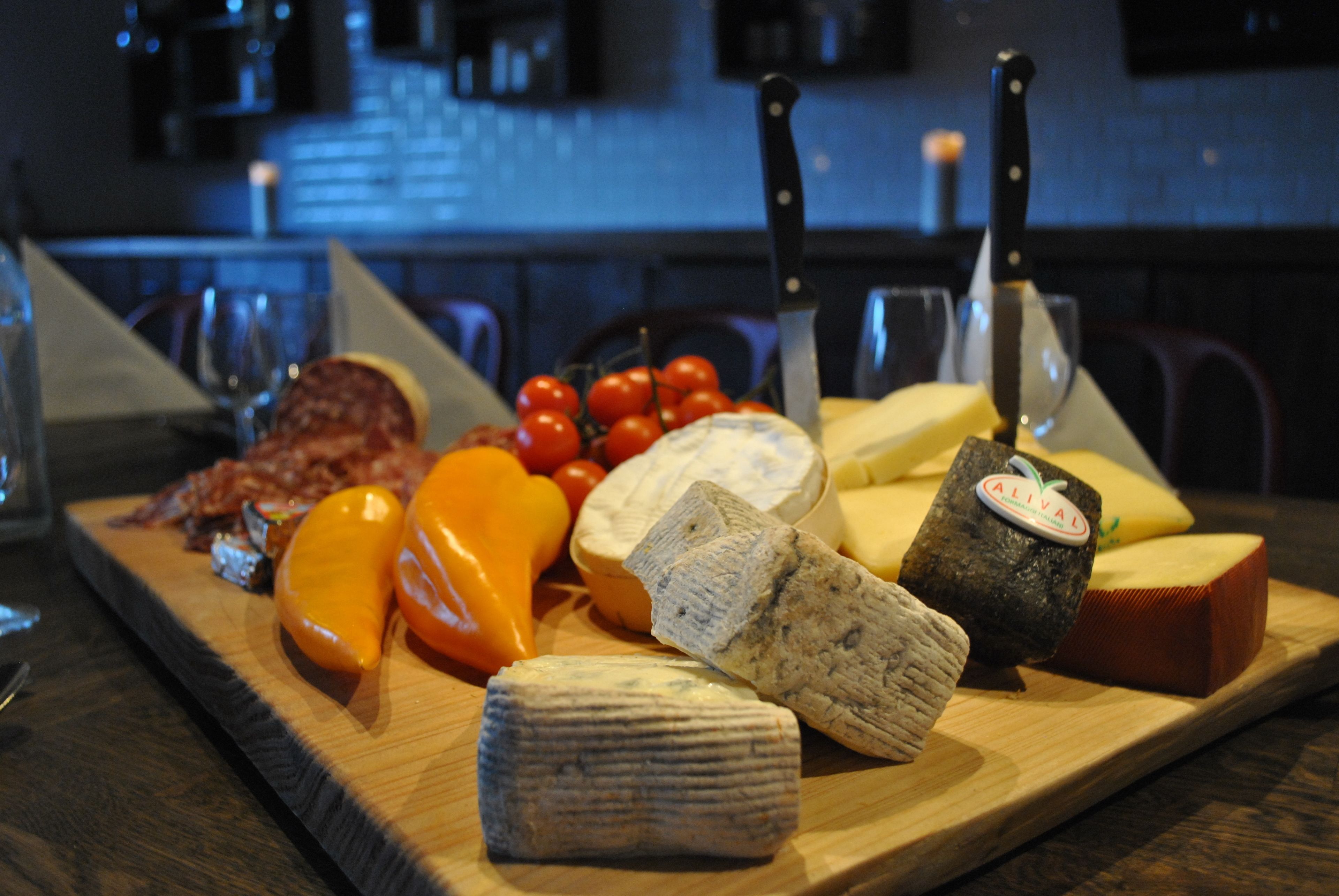 A wooden board with various cheeses, tomatoes, and a knife.