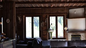 Un interior rústico con paredes de madera, chimenea de piedra, sofás de cuero y ventanas amplias con vistas al follaje.