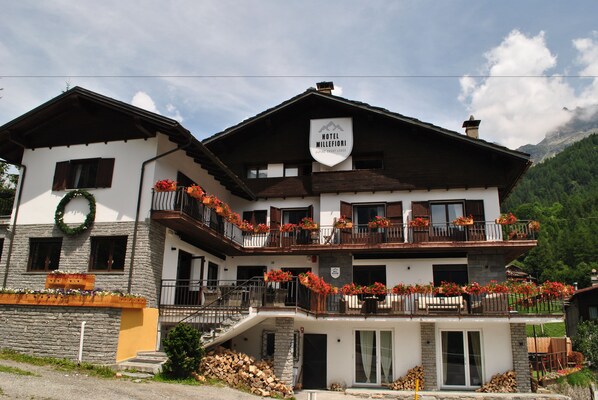 Ein zweistöckiges Hotel mit Balkonen, die mit Blumen geschmückt sind, einer Steinfassade und einem Schild, das es als Hotel kennzeichnet.