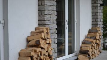 Una pila de leña apoyada contra una pared de piedra junto a una puerta de vidrio.