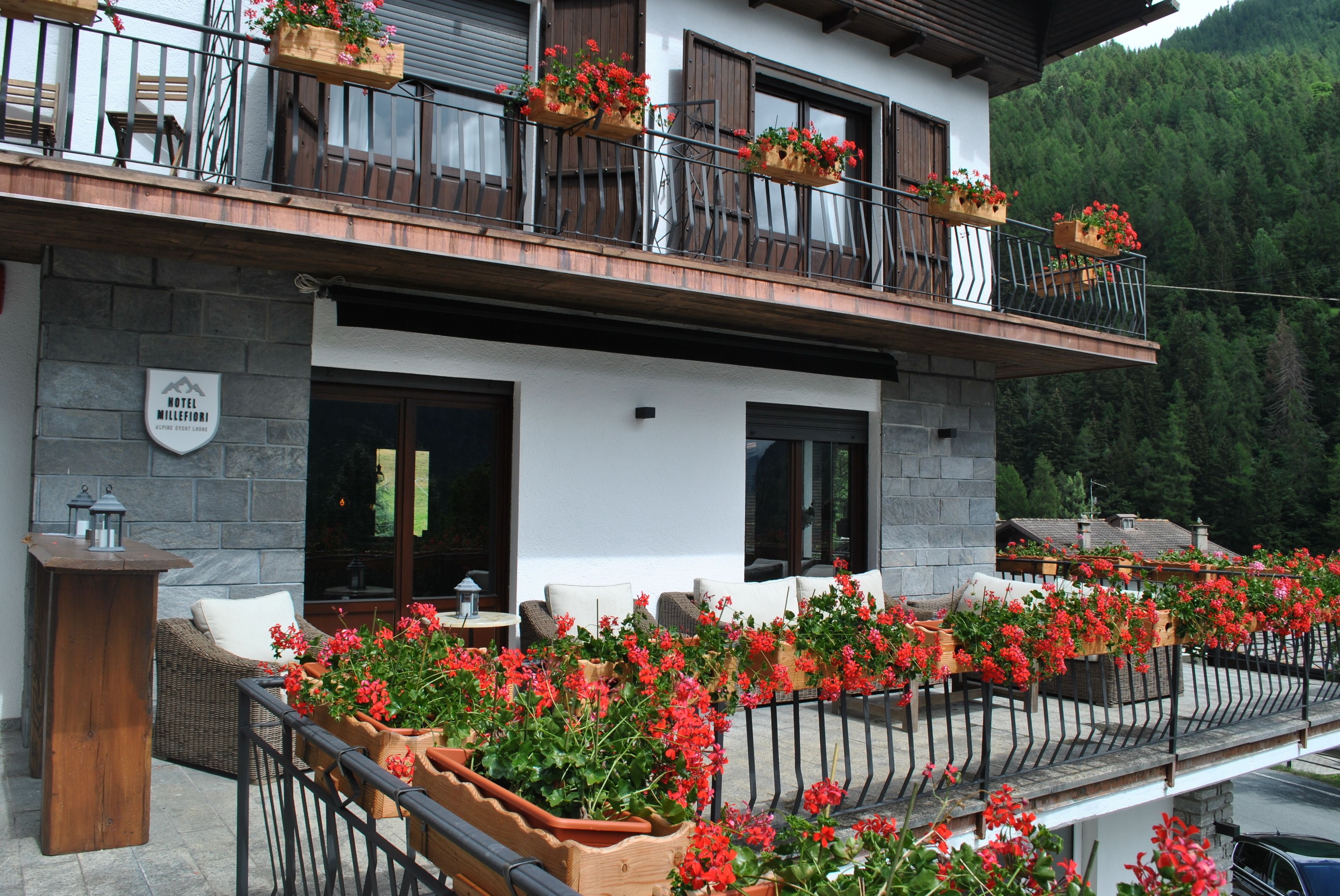 Un hotel con terraza, jardineras en el balcón y fachada de piedra.